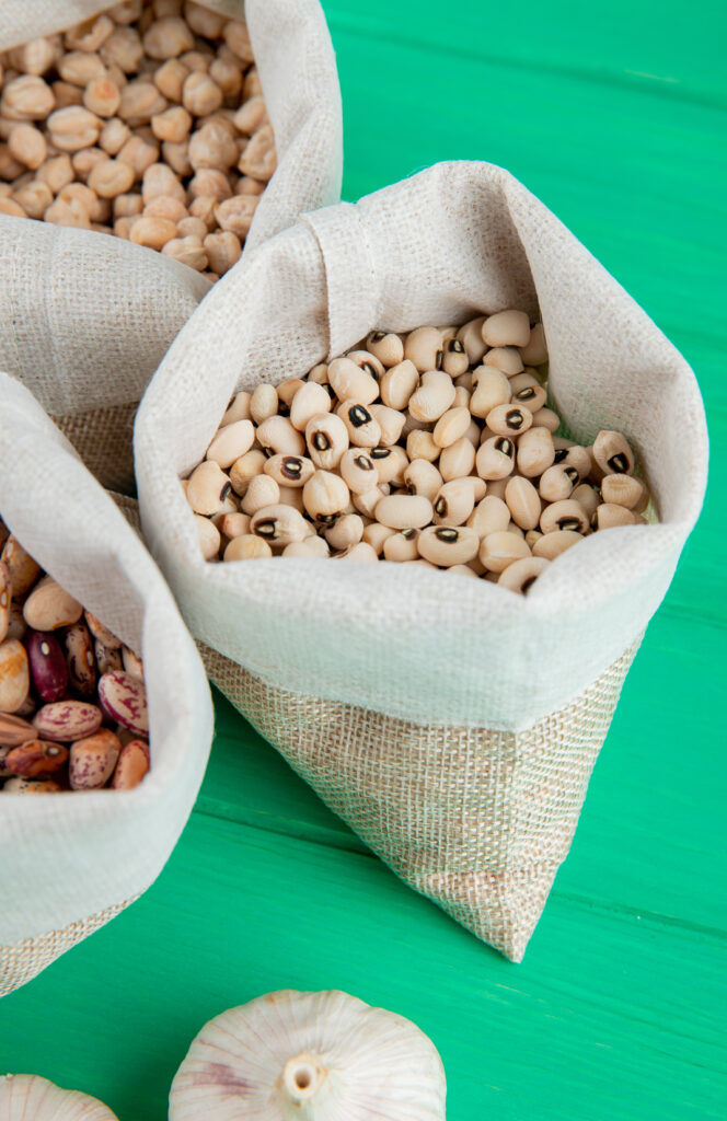 side view of various types of beans lined up in sacks on green wooden background